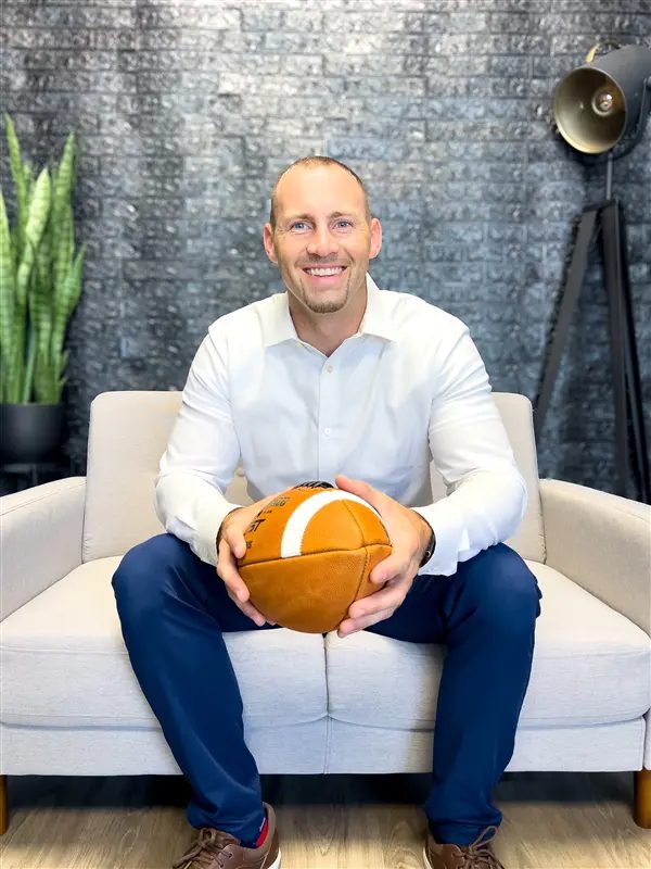 Dr. Nick portrait, seated on couch holding a football